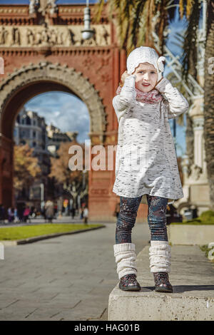 A Barcellona per una perfetta inverno. A piena lunghezza ritratto della ragazza alla moda vicino al Arc de Triomf a Barcellona Spagna tenendo il suo cappello Foto Stock