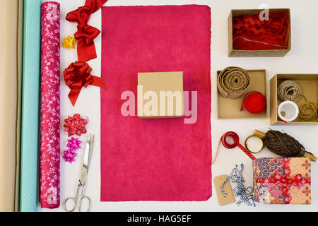 Alta angolazione di un tavolo bianco pieno di scatole, la carta di avvolgimento con diversi modelli e colori e stringhe e nastri di diversi colori Foto Stock