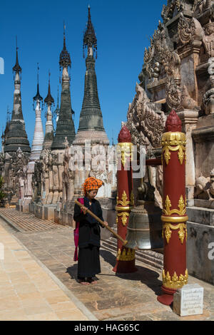 Una donna del popolo PaO lo squillo di un tempio campana in Kakku tempio Buddista nello Stato di Shan in Myanmar (Birmania). Foto Stock