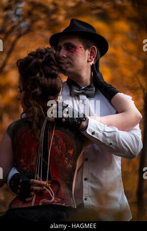 Giovane uomo ad imitazione delle prestazioni musicali sulla donna torna con il dipinto di violoncello. Colorato parco di alberi sullo sfondo Foto Stock