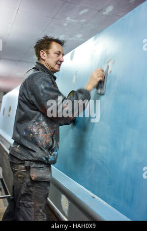 Andy Russell narrowboat pittore al lavoro di levigatura sottosmalto in giù su un narrowboat Foto Stock