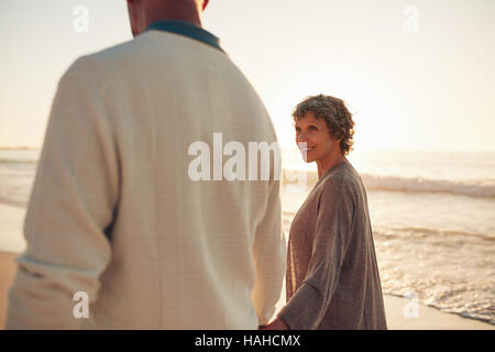 Sorridente donna senior con suo marito a piedi lungo la spiaggia. Coppia matura a camminare insieme sulla riva del mare. Foto Stock