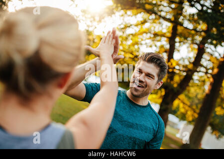 Un colpo di giovane uomo in forma che dà cinque in alto alla donna. una coppia di fitness nel parco dà cinque alti. Foto Stock