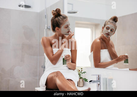 Giovane donna seduta in bagno e applicando facepack. Bellissima femmina nella parte anteriore dello specchio di applicare la maschera facciale. Foto Stock