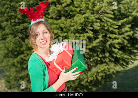 Bellissima ragazza con le orecchie di renne azienda presenta nella parte anteriore del grande abete Foto Stock