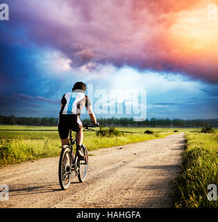 Uomo in sella a una moto sulla strada di campagna al tramonto Foto Stock