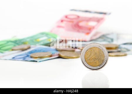 Due monete in euro con altre monete metalliche e delle banconote in euro in background Foto Stock