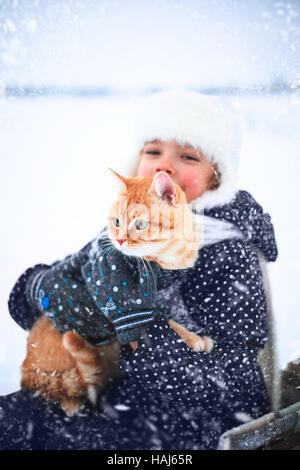 Bambina tiene un gatto rosso nelle sue mani seduto su una slitta in inverno. Foto Stock