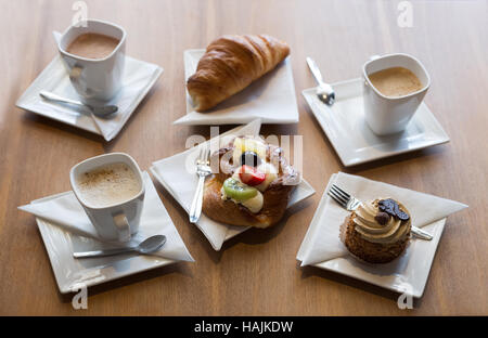 Ancora in vita. Tre tazze di caffè, croissant e pasticcini. Su un tavolo di legno. Foto Stock