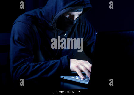 Hacker con maschera utilizzando il computer portatile Foto Stock