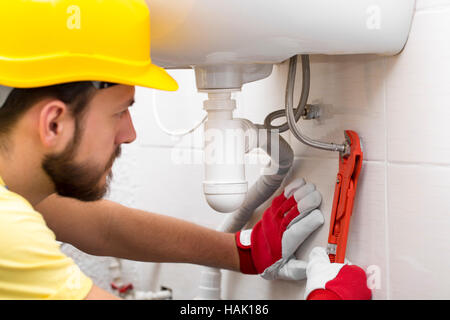 Plumber dissipatore di fissaggio tubazione con chiave in bagno Foto Stock