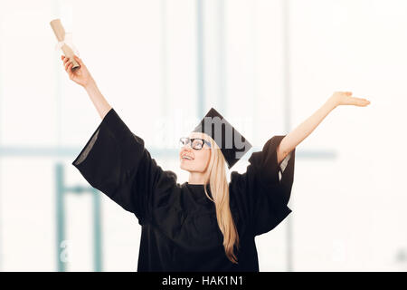 Felice laureato che indossa il cappello e camice e tenendo il diploma in mano Foto Stock