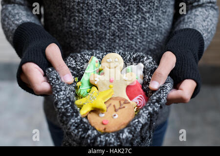 Primo piano di un giovane uomo caucasico indossando i guanti che tiene nelle sue mani una calza a maglia piena di biscotti di Natale con diverse forme e colori Foto Stock