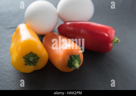 Low Carb - due uova di colore bianco con tre mini colorati paprikas al buio su un sfondo di ardesia - vivida luce. Foto Stock