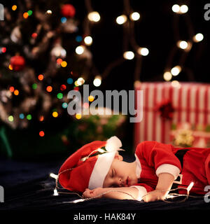 Il bambino dorme nella santa costume con decorazioni di Natale come bokeh di fondo Foto Stock