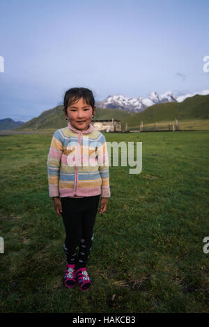 Giovani felici bambina nel cortile della sua famiglia's yurt tenda a 3000 m di altitudine, vicino alla frontiera cinese, Kirghizistan Foto Stock