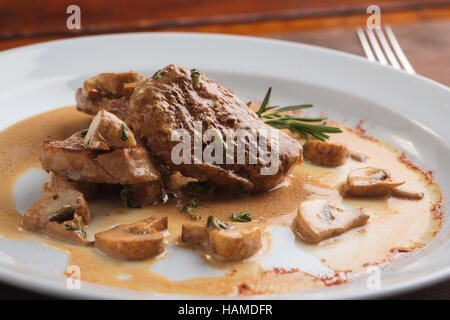 Concetto: ristorante menu, mangiare sano, fatti in casa, golosi, golosità. Piastra bianca di medaglioni di maiale con salsa di funghi su weathered tavolo in legno Foto Stock