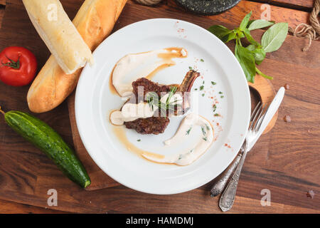 Concetto: ristorante menu, mangiare sano, fatti in casa, golosi, golosità. Piastra bianca di agnello cremagliera sul tavolo di legno e gli ingredienti su sfondo. Top- Foto Stock