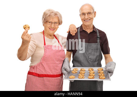 Uomo anziano tenendo un vassoio di biscotti appena sfornati e una donna anziana tenendo un cookie unico isolato su sfondo bianco Foto Stock