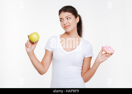 Foto di giovane donna scegliendo tra ciambella e Apple. Isolato su sfondo bianco. Foto Stock