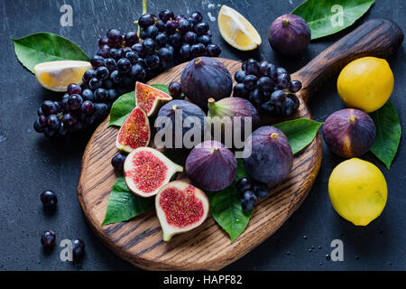 Fichi freschi, uva nera e limoni. Frutta fresca varietà sul tagliere di legno Foto Stock