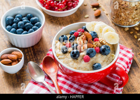 Una sana prima colazione, fiocchi d'avena porridge con frutta fresca e bacche, dadi e muesli su tavola in legno rustico. Vista ravvicinata Foto Stock