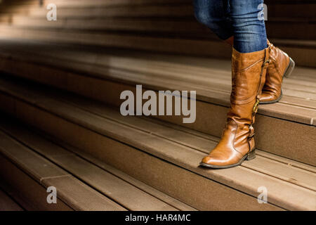 Giovane donna in stivali in pelle in piedi sulle scale di legno di notte Foto Stock