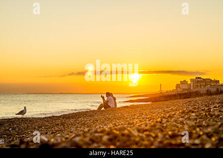 Giovane seduto da solo su una spiaggia rocciosa al tramonto Foto Stock