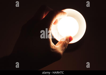 Maschio girando a mano sulla piccola lampada al tungsteno in metallo paralume su sfondo nero, closeup photo Foto Stock