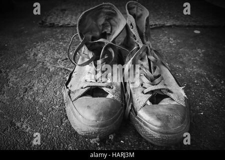 Vecchio sneakers stare in piedi sul pavimento di cemento. Closeup foto in bianco e nero Foto Stock