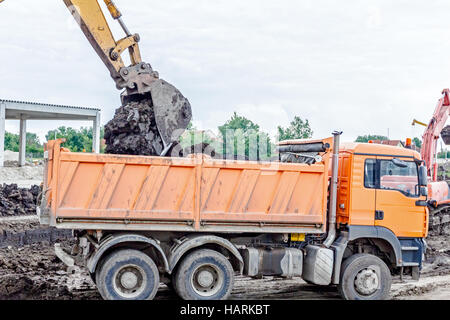 Escavatore giallo è il riempimento di un autocarro con cassone ribaltabile con terreno in corrispondenza del sito di costruzione, il progetto in corso. Foto Stock