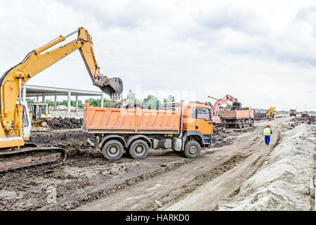 Escavatore giallo è il riempimento di un autocarro con cassone ribaltabile con terreno in corrispondenza del sito di costruzione, il progetto in corso. Foto Stock