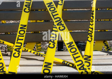 Una panchina nel parco avvolto con giallo Nastro di avvertenza. Foto Stock