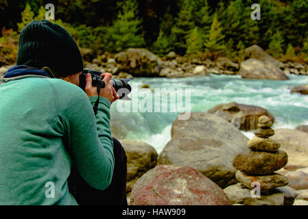 Signora o donna prendendo foto di cairn pila di rocce su riverside in Nepal, HIMALAYA, vicino a phakding Foto Stock