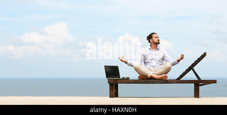 Imprenditore indossa una tuta sulla sedia a sdraio fare yoga sulla spiaggia Foto Stock
