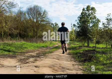 Grande pancia uomo jogging , esercitare, facendo cardio nel parco , leggermente sovrappeso, perdere peso. In un prato di erba verde tra alberi senza lea Foto Stock