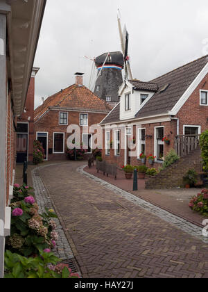 Strada di ciottoli con case tradizionali e un mulino a vento nel villaggio di Winsum, Paesi Bassi Foto Stock