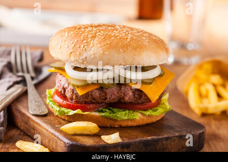 Appetitosi hamburger con patatine fritte, birra sul tagliere di legno. Pickles, cipolla e formaggio cheddar. Foto Stock