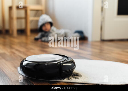 Robotica aspirapolvere sul piccolo tappeto bianco con baby boy sullo sfondo Foto Stock