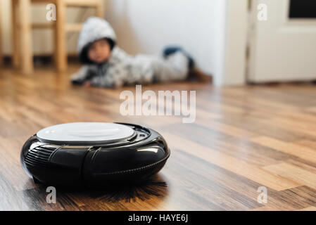 Robotica aspirapolvere sul pavimento in laminato con baby boy sullo sfondo Foto Stock
