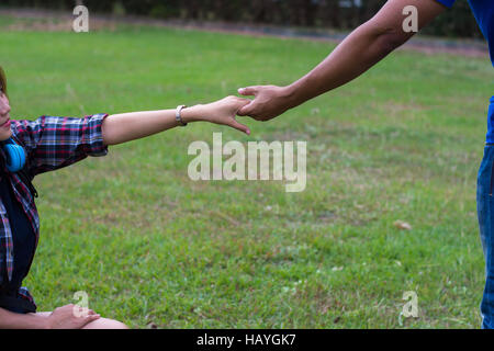 Donna seduta sull'erba raggiungendo a scuotere la mano dell'uomo. mano e concetto di amore. Foto Stock