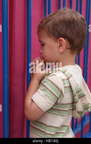 Moody little boy in piedi dal gate colorati Foto Stock