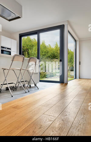 Pavimento in legno in un moderno appartamento interno con finestre francesi e un lussureggiante giardino Foto Stock