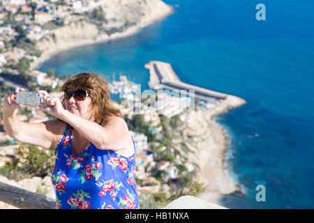 Donna prendendo selfie alto con vista di Calp, Calpe porto e di urbanizzazione di Maryvilla, Peñón de Ifac Parc Natural Foto Stock