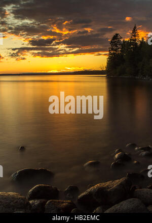 Moody tramonto con acqua setosa, rocce in primo piano. Foto Stock