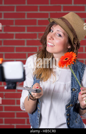 Ragazza tenendo selfie di fronte a un muro di mattoni Foto Stock