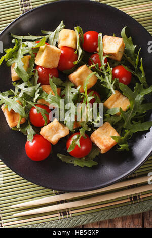 Insalata: tofu fritto con pomodori e rucola fresca close-up su una piastra sul tavolo. vista verticale da sopra Foto Stock