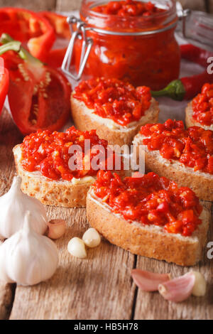 Messa a fuoco selettiva sull'ajvar sul grano intero pane closeup sul tavolo. In verticale Foto Stock