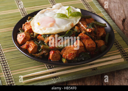 Stir-Fry piccante di pollo con basilico, fagioli verdi e un uovo fritto su una piastra di close-up orizzontale Foto Stock