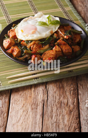 Stir-Fry piccante di pollo con basilico, fagioli verdi e un uovo fritto su una piastra di close-up verticale Foto Stock